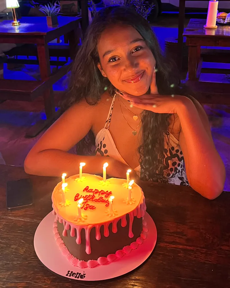 Cliente da Hello Confeitaria sorrindo atrás do bolo de coração com as velas acesas